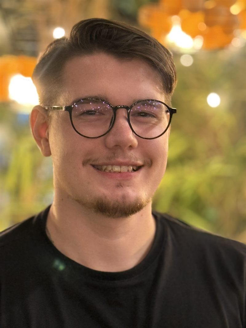 André Cordeiro smiling, wearing glasses and a black t-shirt.
